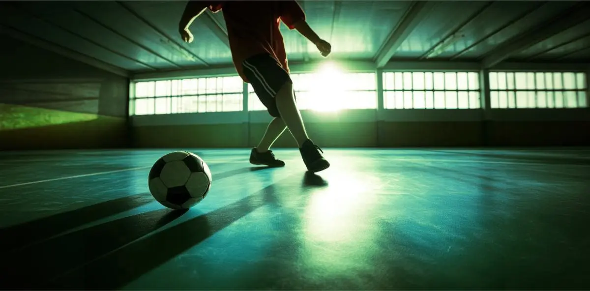 Young player practices soccer indoors evening casting long shadows green court